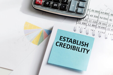 ESTABLISH CREDIBILITY text on a blue card on the background of documents, calculator on the table