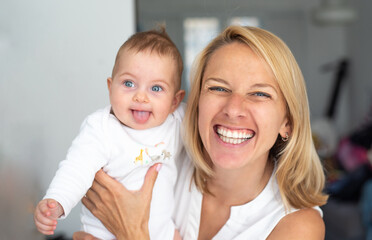 Sweet little baby-girl with blue eyes is held on her mather’s arms, laughs and enjoy love. positive emotions. close up view. 