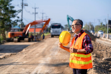 The foreman, wearing a safety vest, takes off his helmet, takes a break to drink water after supervising workers and road-building machinery at the job site.