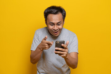 excited Asian man looking and pointing in to smartphone.