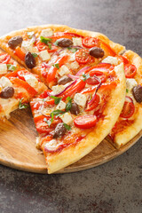 Vegetarian Greek pizza with peppers, feta, onions, tomatoes, olives and herbs close-up on a wooden board on the table. Vertical