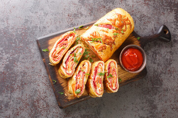 Italian stromboli, delicious pizza roll filled with sausage and ham closeup on the wooden board on...