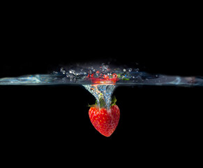 Red strawberry fruit falling in water splash on black background. The bright red fruit sits under clear, bubbly water.