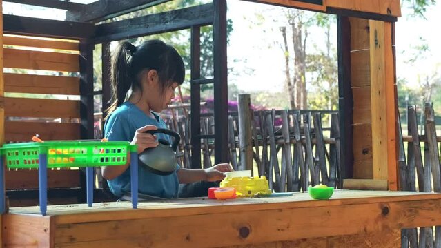 Two happy sisters play with food and wooden grocery toys at the outdoor playground with her mother. Cute Asian girl roleplaying selling fruit juice at the park. Family spending time together on vacati