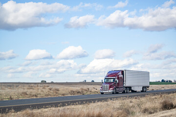 Bonnet burgundy big rig semi truck transporting cargo in refrigerator semi trailer driving on the...