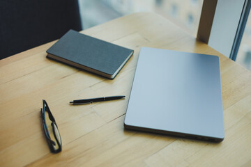 A wooden table with a laptop and a notepad, glasses and a pen. View from above. Place for text