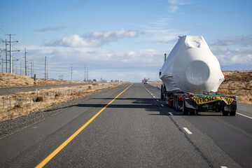 Long hauler big rig semi truck transporting oversize load on the step down semi trailer running on...