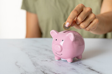 Close-up of a woman's hands putting a euro coin in a piggy bank, saving money in a crisis and inflation