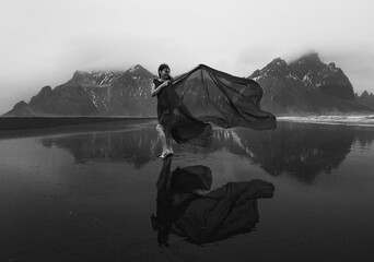 Elegant lady wrapped with chiffon on beach monochrome scenic photography. Picture of person with mountains on background. High quality wallpaper. Photo concept for ads, travel blog, magazine, article