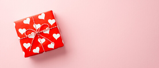 Valentine's Day concept. Top view photo of giftbox in wrapping paper with heart pattern on isolated pastel pink background with copyspace
