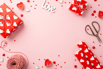 Valentine's Day concept. Top view photo of gift boxes hearts candles wrapping paper roll spool of twine scissors and sprinkles on isolated pastel pink background with copyspace in the middle