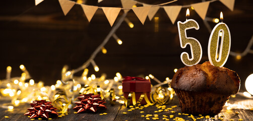 Number 50 golden festive burning candles in a cake, wooden holiday background. fifty years of...