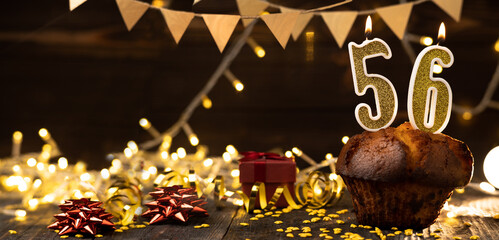 Number 56 golden festive burning candles in a cake, wooden holiday background. fifty-six years since the birth. the concept of celebrating a birthday, anniversary, holiday. Banner.
