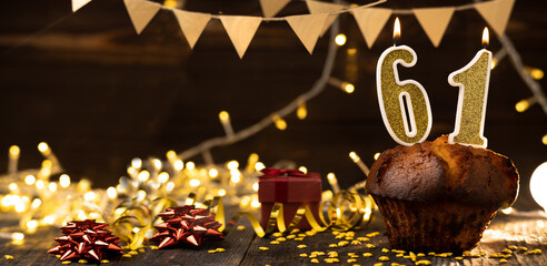 Number 61 golden festive burning candles in a cake, wooden holiday background. sixty-one years...