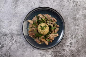 Pork stew with mushrooms and bulgur on a round plate on a dark background. Top view, flat lay