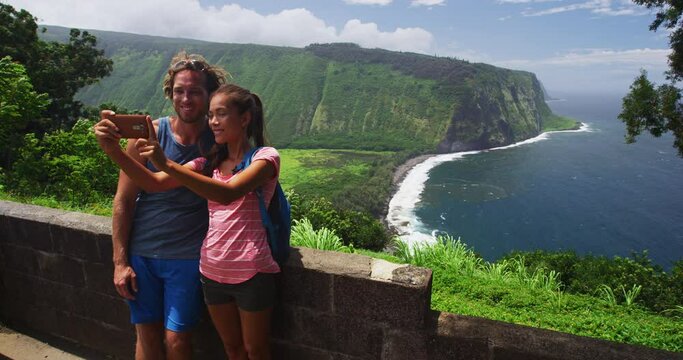 Hawaii Big Island tourists couple taking phone selfie photo at Waipio Valley Lookout. Couple on travel