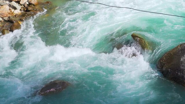 Closeup shot of river Parvati flowing rapidly at Kasol in Himachal Pradesh, India. Clear blue colored river running in between the Himalayan mountains in India. Natural Himalayan river background.