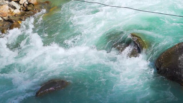 Slow motion shot of river Parvati flowing rapidly at Kasol in Himachal Pradesh, India. Clear blue colored river running in between the Himalayan mountains in India. Natural Himalayan river background.
