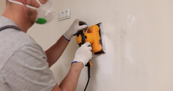 Home improvement worker in protective mask and goggles works with grinder to level surface of wall