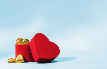 Golden chocolate hearts in and near red velvet heart box on blue background. St Valentines or...