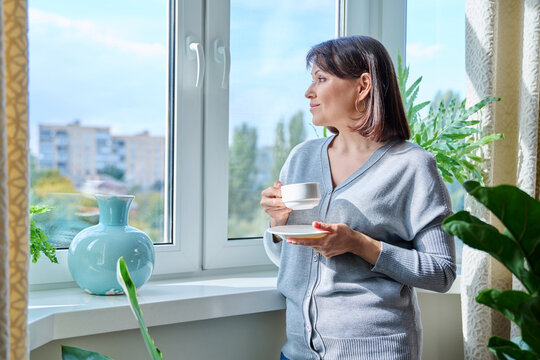 Smiling Middle Aged Woman With Cup Of Coffee Looking Out Window