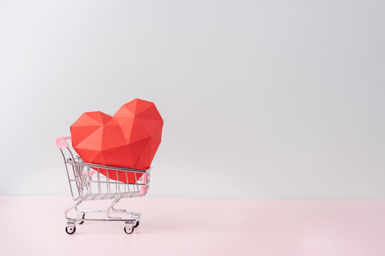 Red paper heart in a shopping cart against blue background.