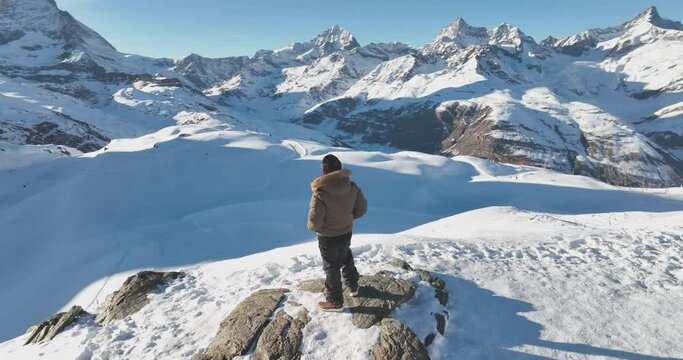 Successful asian man celebrate and raising arms on mountain peak view point with iconic famous Matterhorn background. Swiss alps, Switzerland. Travel and Adventure concept. Aerial drone orbit shot.
