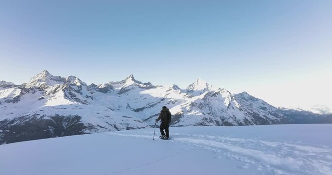 Aerial drone of Young man tourist hiker walking in snow shoes. Successful climber hiking up to mountain top swiss alps, Switzerland. Active travel lifestyle winter outdoor activities. Slow motion.