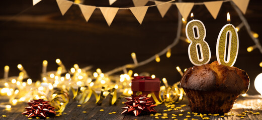 Number 80 golden festive burning candles in a cake, wooden holiday background. Eighty years since the birth. the concept of celebrating a birthday, anniversary, holiday. Banner.