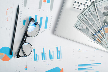 Business documents, laptop, money dollars, glasses and pencil lying on desktop, top view. Economy,...