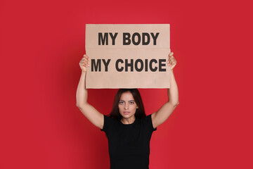 Woman holding placard with phrase My Body My Choice on red background. Abortion protest