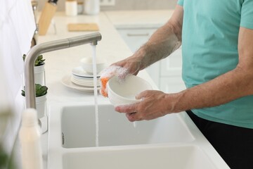 Man washing bowl above sink in kitchen, closeup