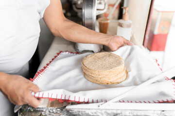 An adult tortilla maker is covering the warm corn tortillas with cloth during a sale