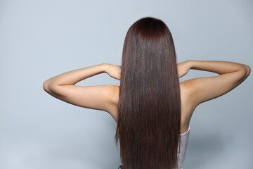 Young woman with healthy strong hair on light gray background, back view