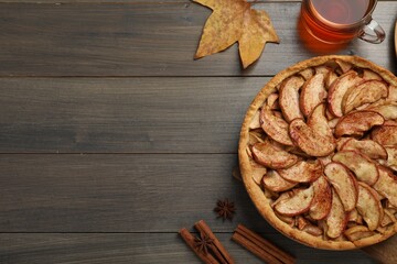 Fototapeta premium Delicious apple pie, cup of tea and cinnamon on wooden table, flat lay. Space for text