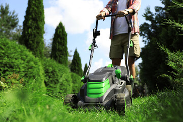 Man cutting grass with lawn mower in garden on sunny day, closeup