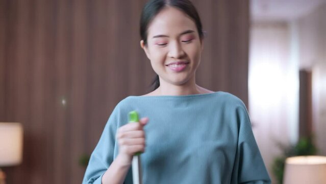 Happy young asian casually cloth woman housewife vacuuming and cleaning floor, singing with cheerful enjoy, and dancing in the living room at home house work weekend activity