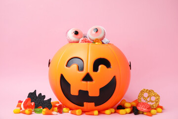 Fototapeta premium Halloween trick or treat bucket with different sweets on pink background
