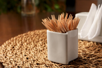 Wooden holder with many toothpicks on wicker mat, closeup. Space for text