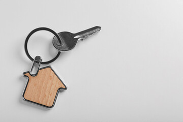 Key with trinket in shape of house on white background, top view and space for text. Real estate agent services