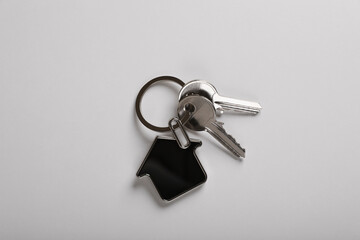 Keys with trinket in shape of house on white background, top view. Real estate agent services