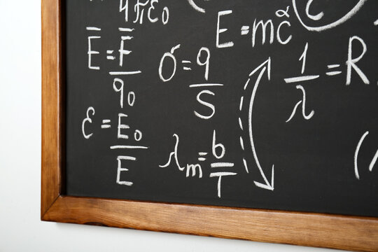 Blackboard with different physical formulas written with chalk on white wall
