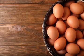 Raw chicken eggs in wicker basket on wooden table, top view. Space for text