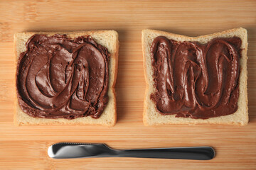 Tasty toasts with chocolate paste served on wooden board, flat lay