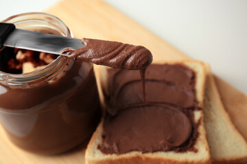 Tasty toast with chocolate paste, knife and jar on wooden board, closeup. Space for text