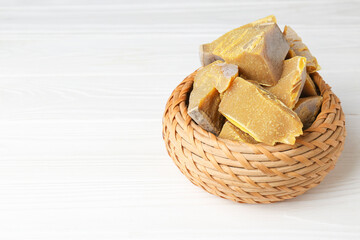 Wicker basket with natural organic beeswax blocks on white wooden table. Space for text