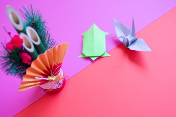 門松と折り紙の鶴と亀と赤背景の写真。門松には迎春と書いてある