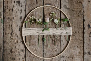 Stylish spring wreath with beautiful fresh flowers. Wooden hoop with flowers and thread on rustic wooden background flat lay. Modern and creative floral handmade decor
