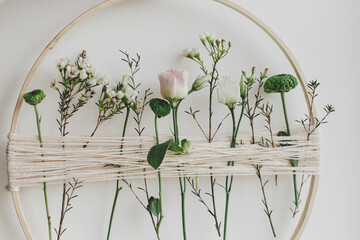 Stylish spring boho wreath with beautiful fresh flowers. Wooden hoop with flowers and thread on...