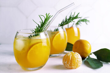 Fresh citrus juice in glasses standing in a row and ripe tangerins. Cold summer drink with citrus slices, ice and rosemary branch on white background. Close up. Selective focus. Blurred background.